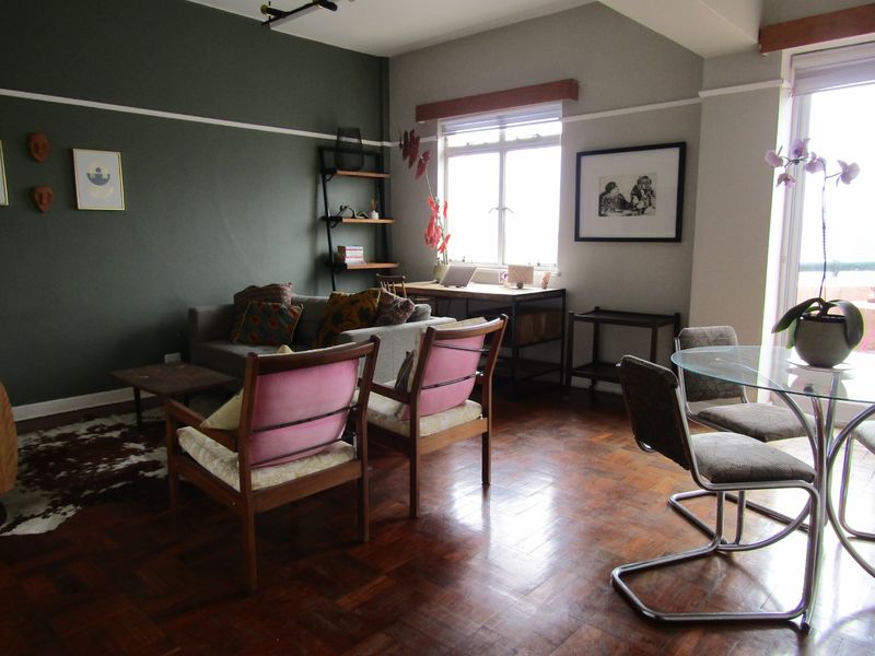 An open-plan living and dining area featuring classic parquet flooring, a decorative picture rail, and access to an outdoor space via a sliding glass door.