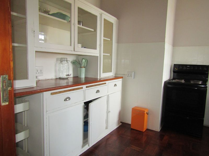 A dated kitchen featuring original white built-in cabinetry with glass display sections, wooden countertops, and a tiled splashback.