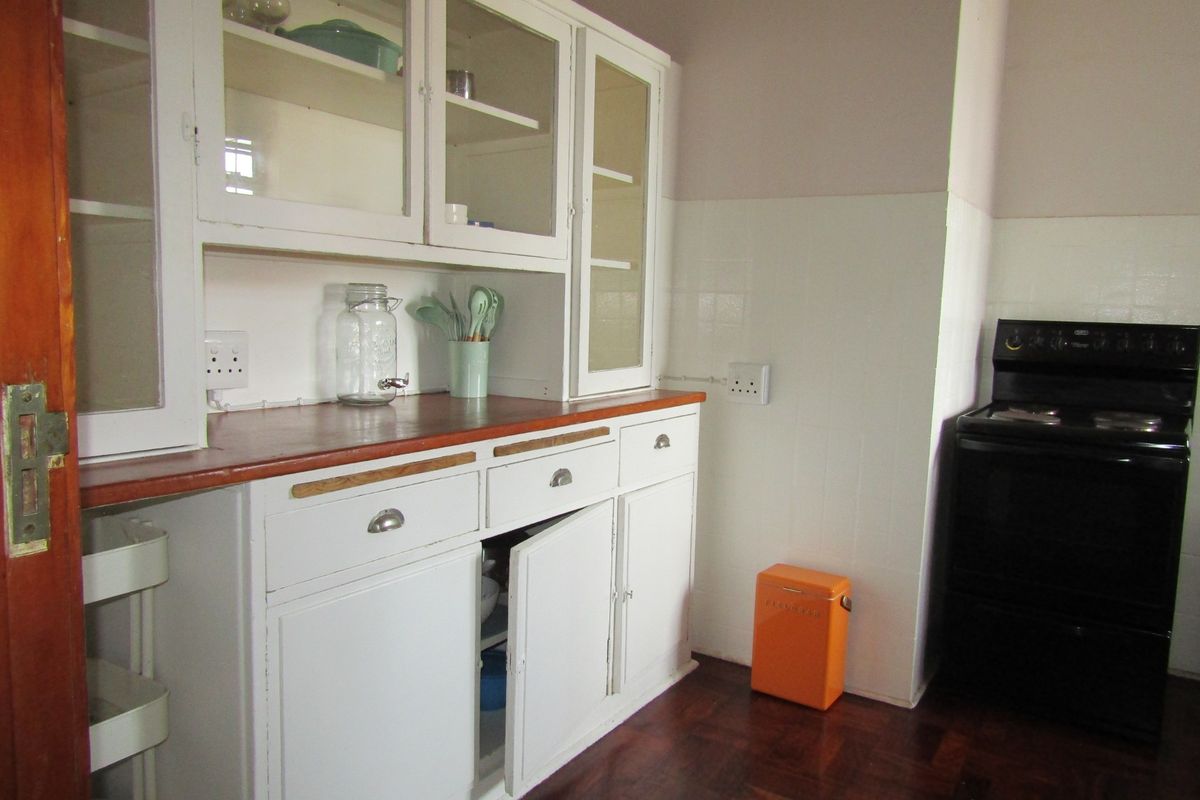 A dated kitchen featuring original white built-in cabinetry with glass display sections, wooden countertops, and a tiled splashback.