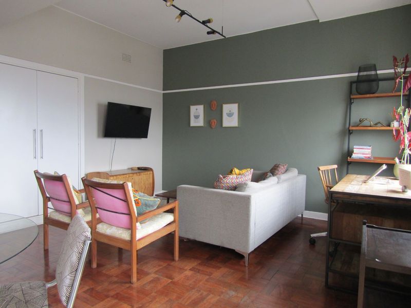 A well-maintained living room featuring classic parquet flooring, a built-in storage cupboard, and a decorative picture rail with modern track lighting.
