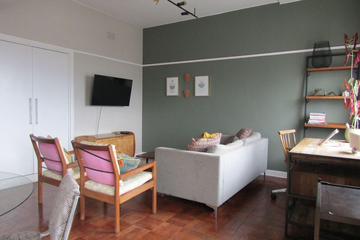 A well-maintained living room featuring classic parquet flooring, a built-in storage cupboard, and a decorative picture rail with modern track lighting.