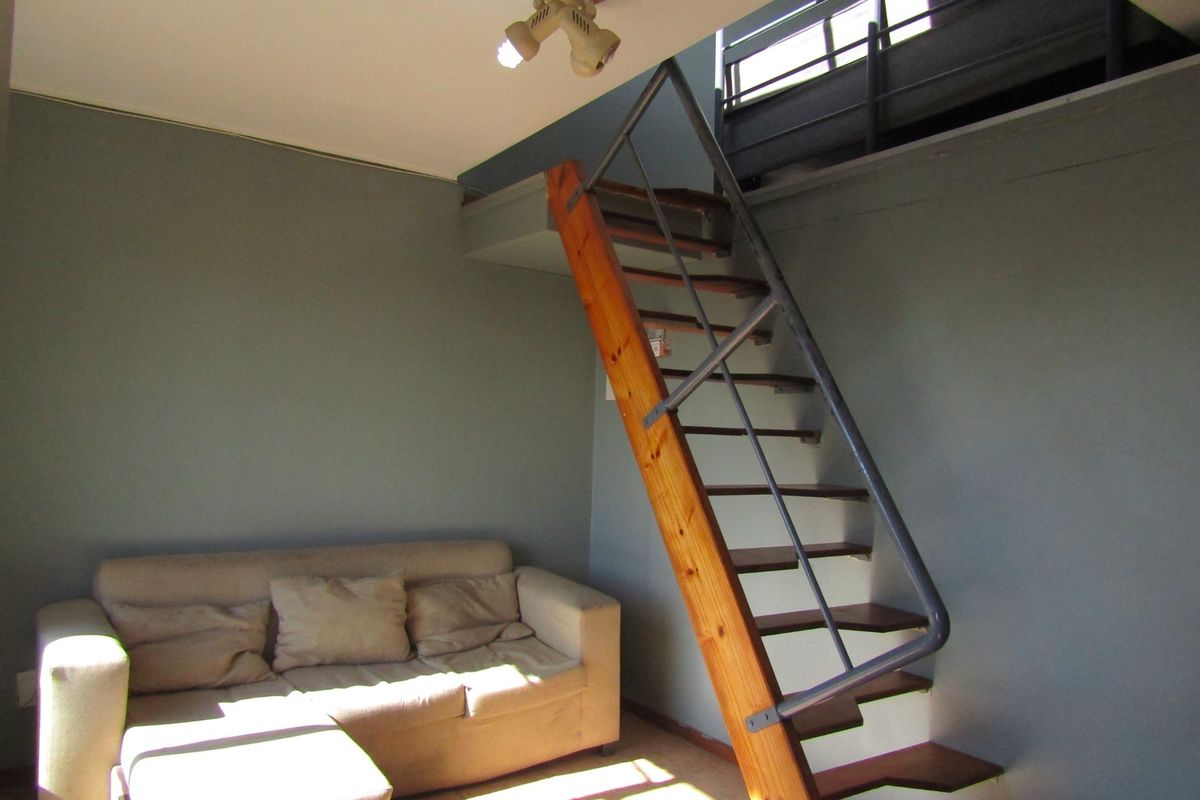Living area featuring a mezzanine level accessed by a timber staircase, tiled flooring, and neutral wall tones.