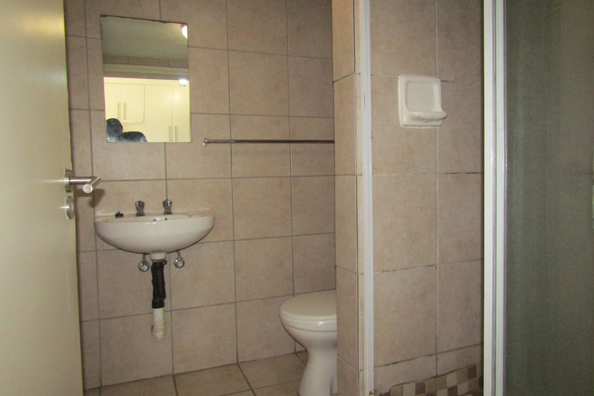 A functional bathroom featuring a wall-mounted basin, toilet, and shower enclosure with neutral wall and floor tiling.
