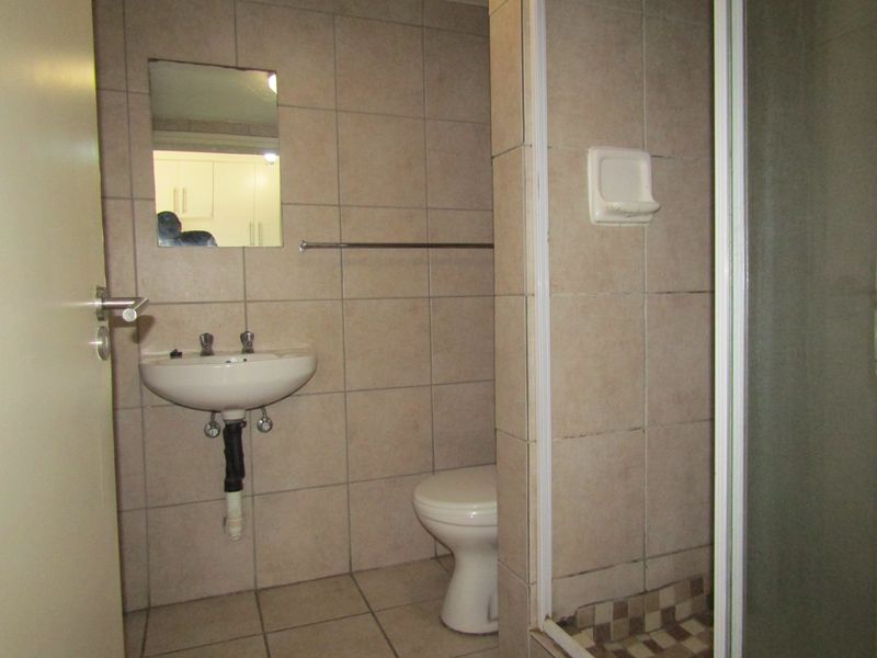 A functional bathroom featuring a wall-mounted basin, toilet, and shower enclosure with neutral wall and floor tiling.