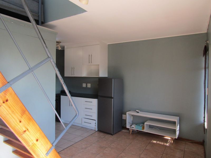 Open plan living area featuring a compact kitchen with white cabinetry, tiled flooring, and a staircase leading to an upper level.