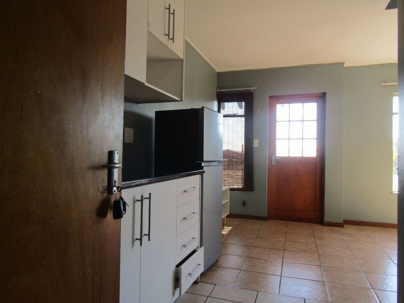 A compact kitchen area featuring built-in cabinetry, dark countertops, and tiled flooring, with direct access to an exterior timber door.