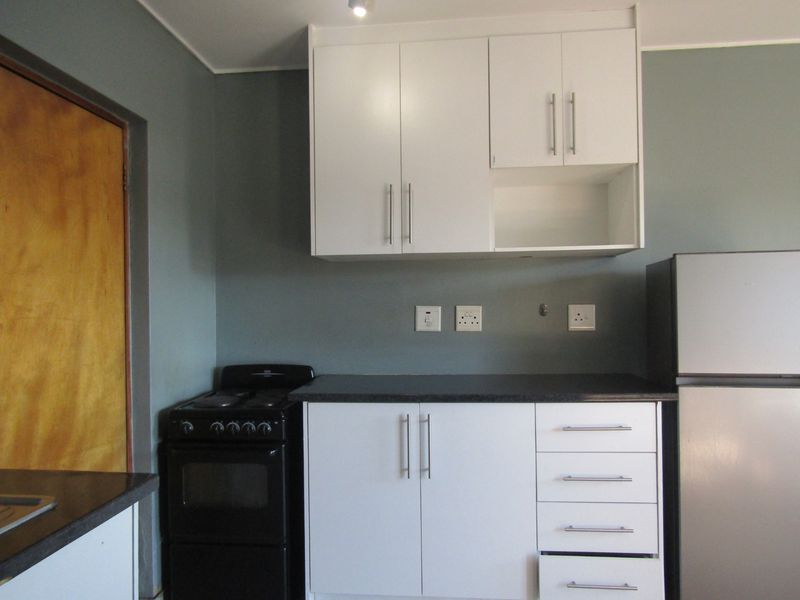 A functional kitchen area featuring white built-in cabinetry, dark laminate countertops, and a freestanding stove, providing a clean and practical workspace.