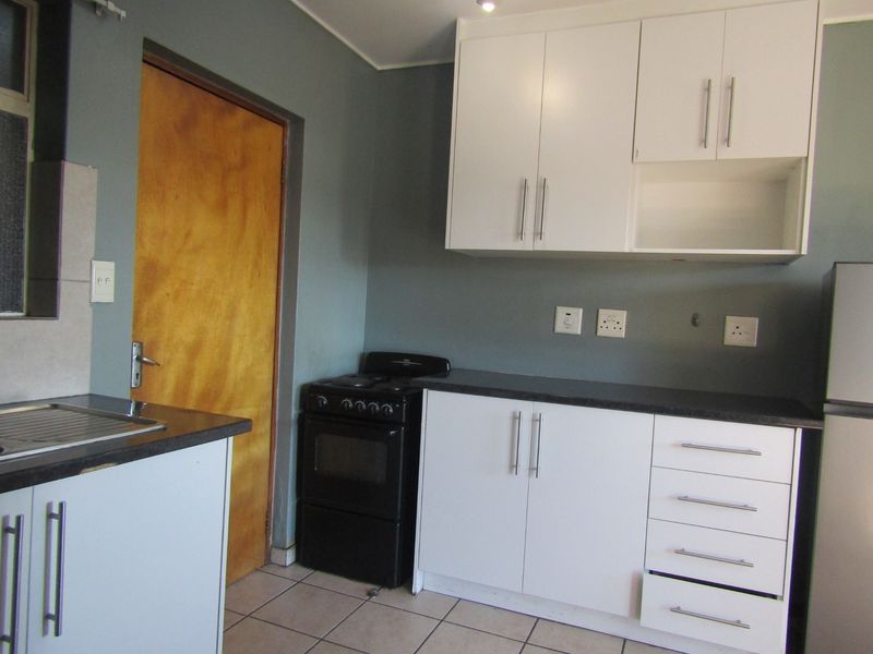 A functional kitchen featuring white cabinetry, dark laminate countertops, a stainless steel sink, and a freestanding stove with tiled flooring.