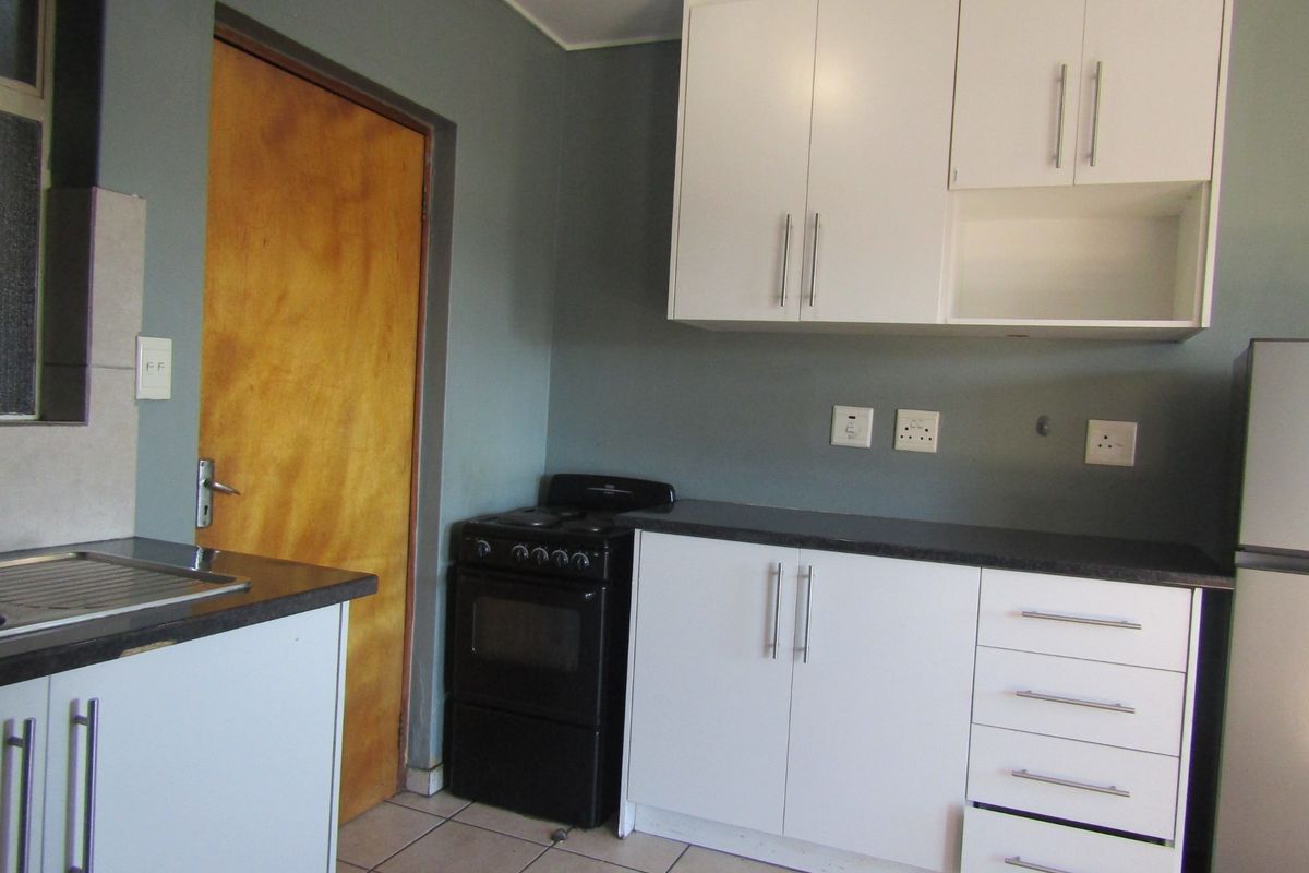 A functional kitchen featuring white cabinetry, dark laminate countertops, a stainless steel sink, and a freestanding stove with tiled flooring.