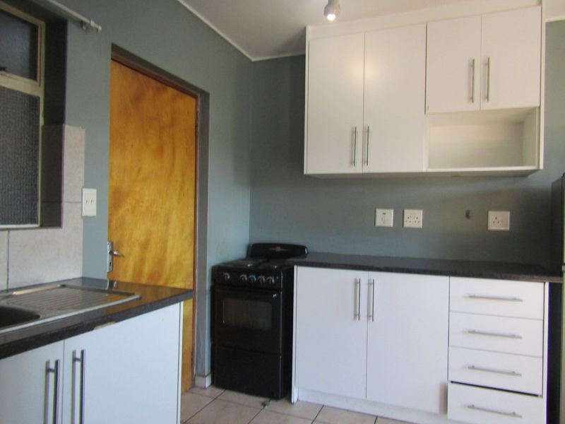 Functional kitchen featuring white cabinetry, dark laminate countertops, tiled flooring, and a freestanding stove, offering a clean and practical workspace.