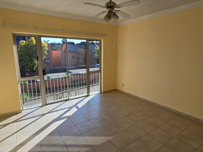 A bright, empty living room featuring tiled flooring, a ceiling fan, and large sliding glass doors that provide natural light and exterior access.