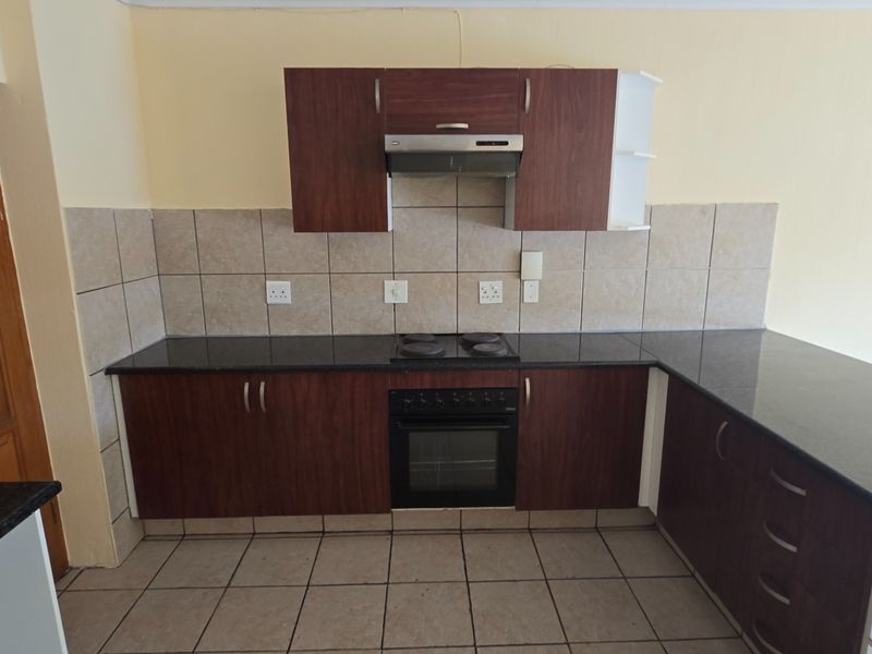 A functional kitchen featuring dark wood cabinetry, granite countertops, a built-in oven, electric hob, and a tiled backsplash.