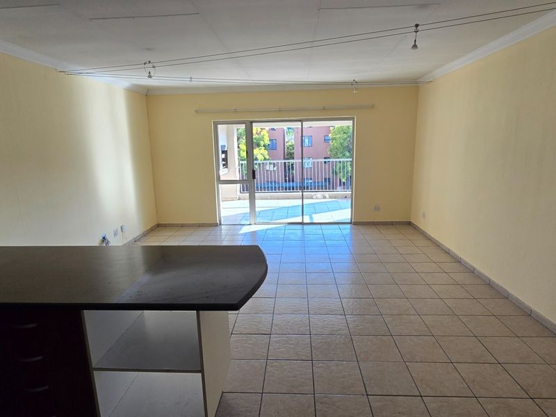 An empty open-plan living area featuring tiled floors, a breakfast bar, and a sliding glass door leading to an outdoor balcony.