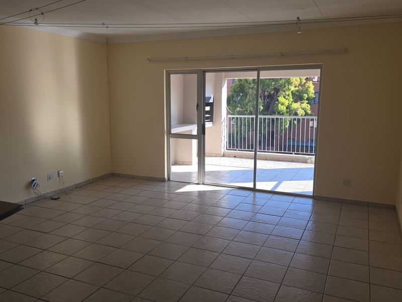 Spacious, empty living area featuring neutral tiled flooring and a large sliding glass door leading to a private balcony with a built-in braai.