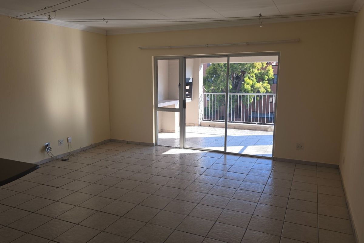 Spacious, empty living area featuring neutral tiled flooring and a large sliding glass door leading to a private balcony with a built-in braai.