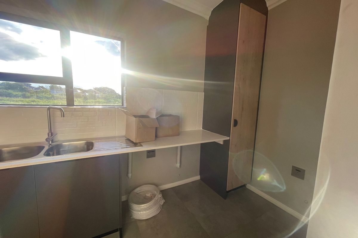 A clean and functional laundry area featuring a stainless steel sink, tiled backsplash, and a tall built-in storage cabinet.