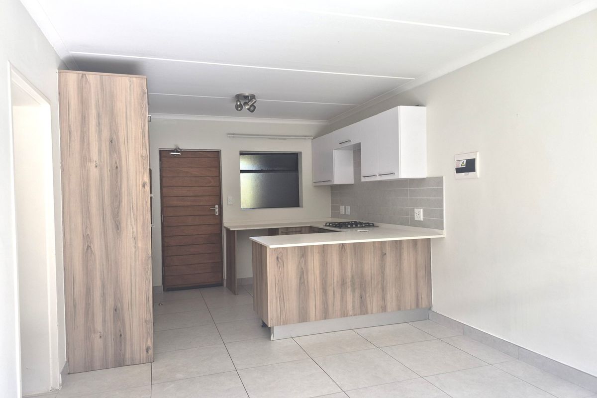 Modern open-plan kitchen featuring light wood-grain cabinetry, white stone countertops, a gas hob, and neutral tiled flooring in a clean, well-maintained space.