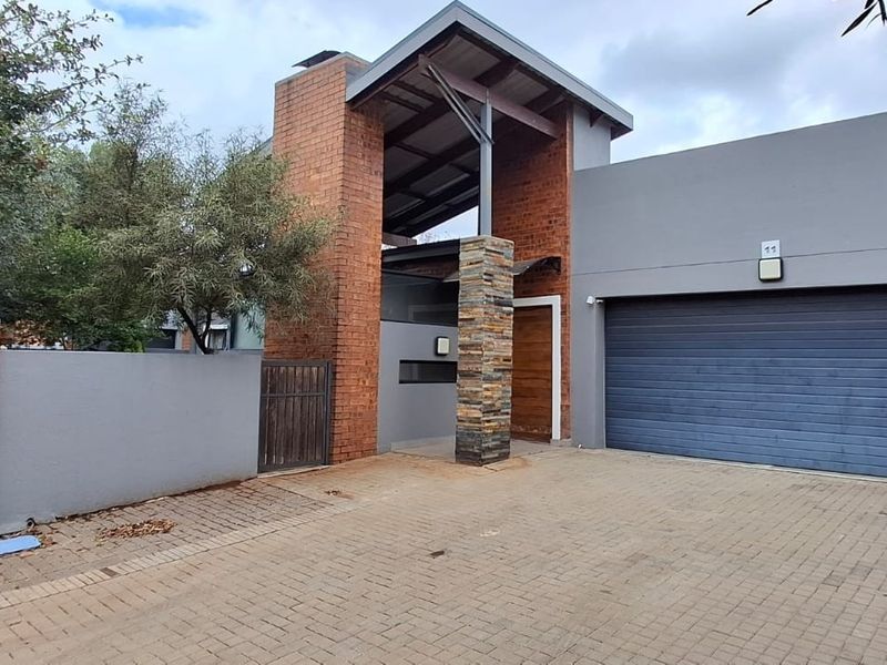 Modern front elevation featuring a combination of brick and stone cladding, an automated garage door, and a paved driveway entrance.
