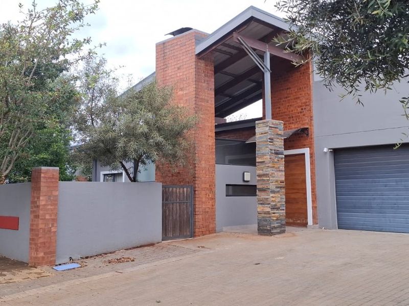 Modern architectural front facade featuring a striking brick chimney, stone-clad pillar, and a secure paved driveway with an integrated garage.