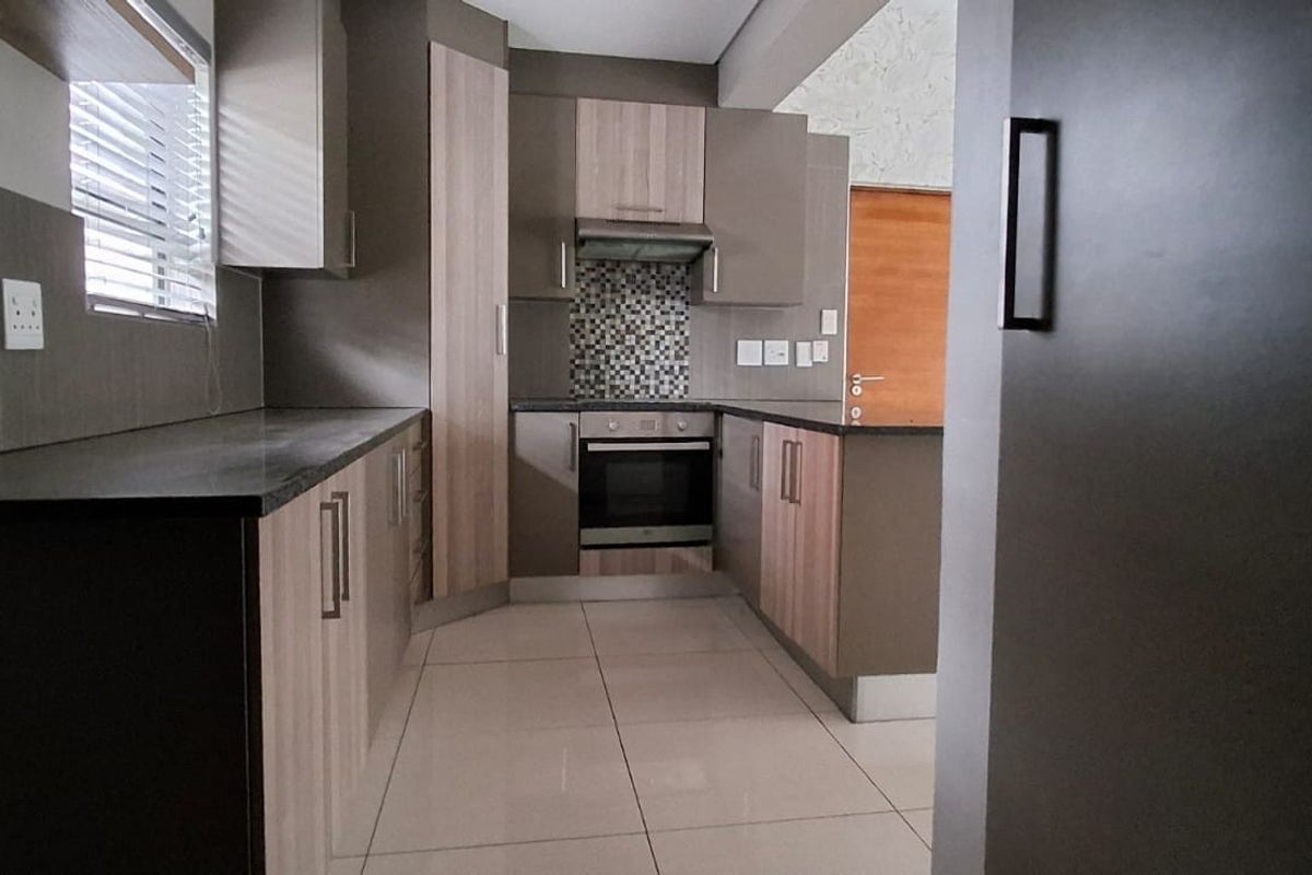 Modern kitchen featuring sleek built-in cabinetry, laminate countertops, a mosaic tile backsplash, and integrated oven with extractor fan, finished with neutral floor tiles.
