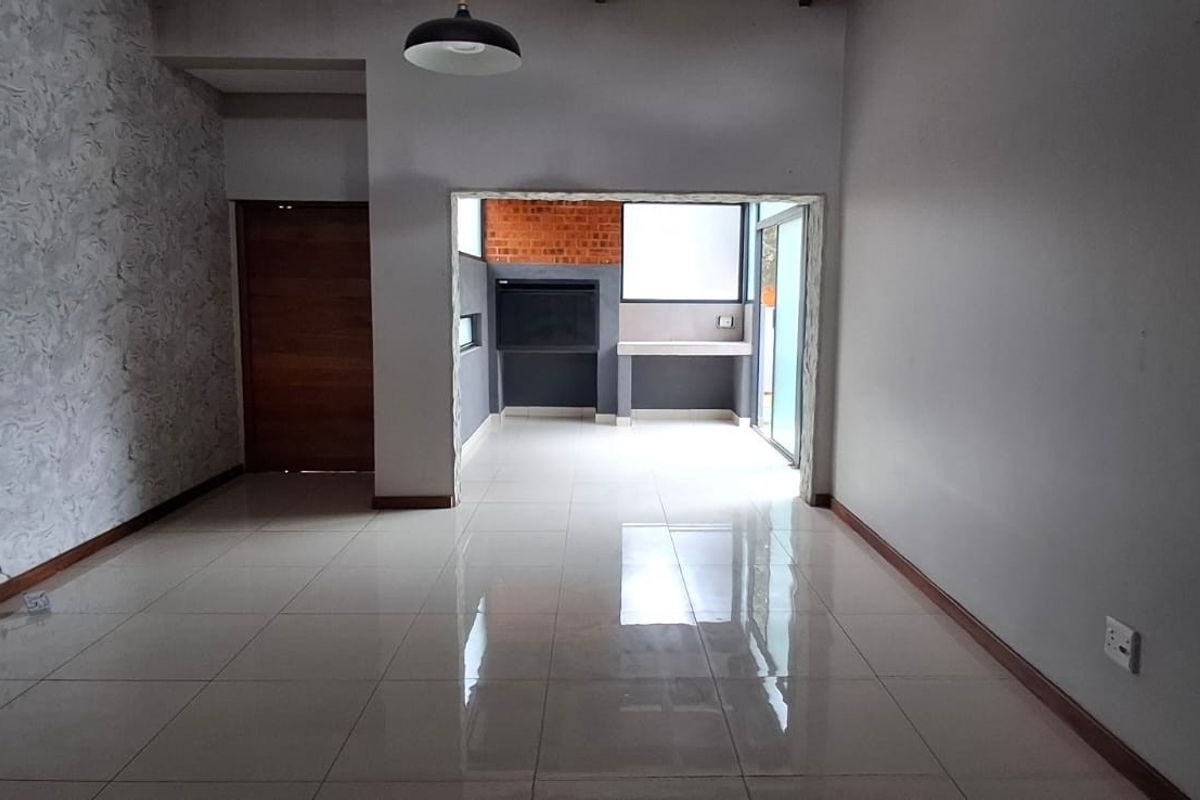 Spacious open-plan living area featuring polished tile flooring, a built-in braai, and direct access to an outdoor patio through sliding glass doors.