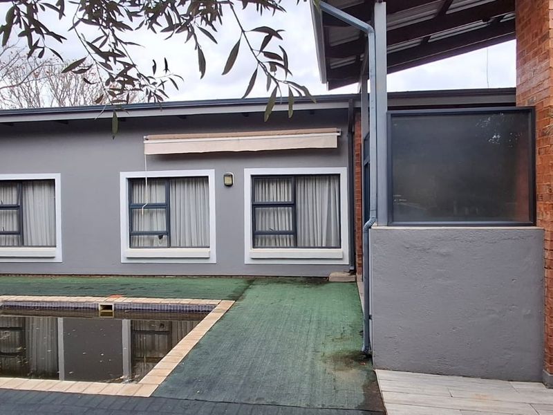 Rear exterior view featuring a swimming pool, brick chimney detail, and grey rendered walls with aluminium window frames.