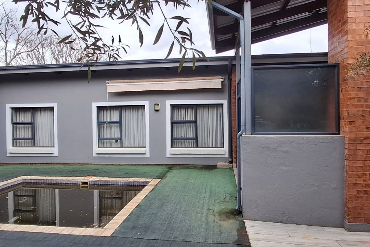 Rear exterior view featuring a swimming pool, brick chimney detail, and grey rendered walls with aluminium window frames.
