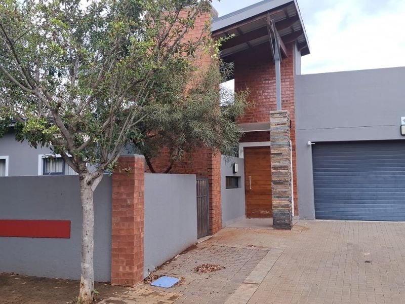 Modern front elevation featuring a combination of brick and grey plaster finishes, stone cladding, a timber entrance door, and a double garage.