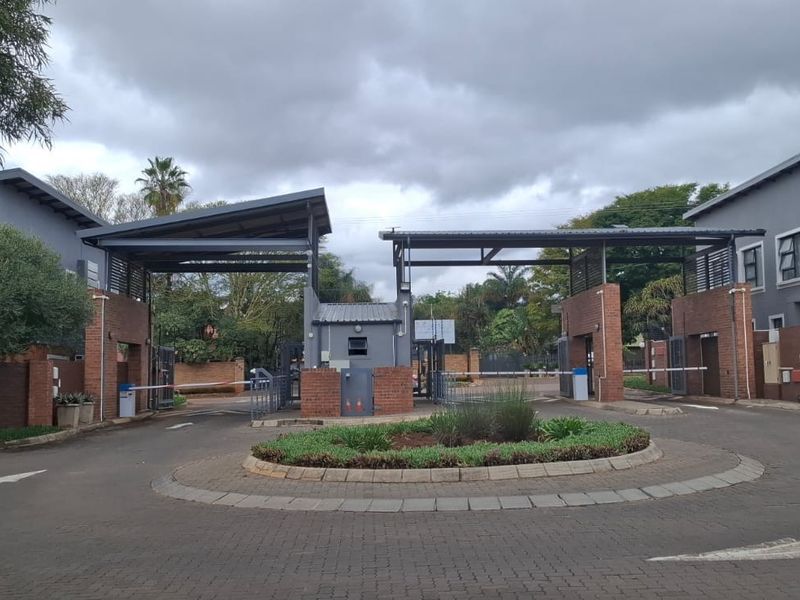 The entrance to the residential estate features a secure gatehouse, boom gates, and a well-maintained paved driveway with landscaped traffic island.
