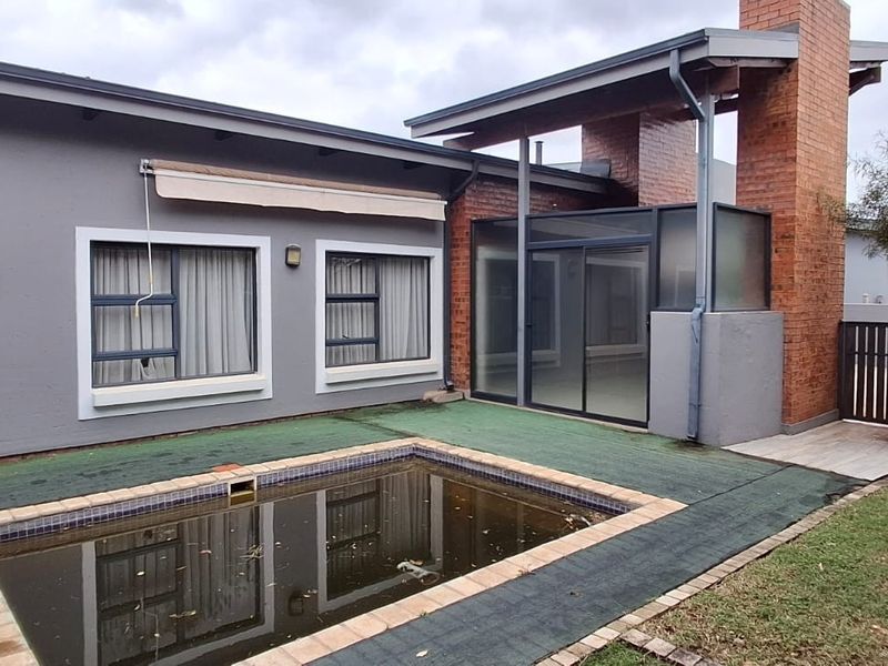 Rear exterior view featuring a swimming pool with a brick chimney structure, sliding glass doors, and a small garden area.