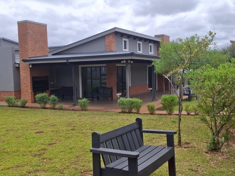 Rear view of the property featuring a covered patio with a built-in braai, sliding door access, and a well-maintained garden area.