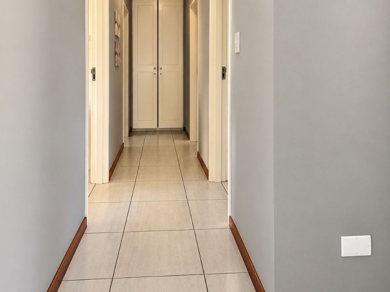 A clean, well-maintained hallway featuring neutral grey walls, tiled flooring, and a built-in storage cupboard at the end.