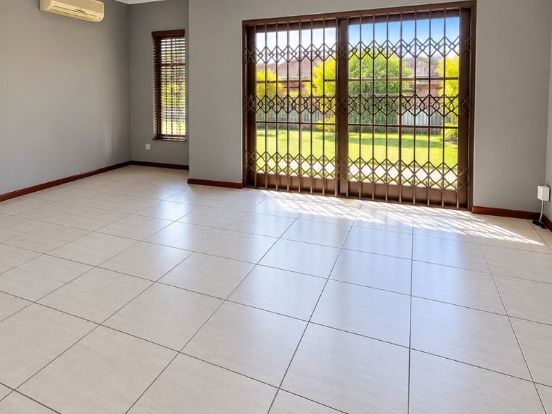 Spacious, empty living area featuring neutral tiled flooring, recessed lighting, a wall-mounted air conditioner, and large sliding doors with security gates leading to the garden.