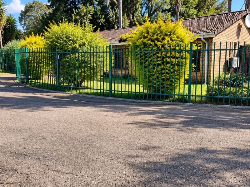 Front view of a brick townhouse featuring a tiled roof, secure metal perimeter fencing, and a landscaped front garden area.