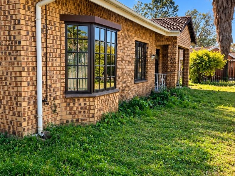 Rear view of a face brick townhouse featuring a bay window, tiled roof, and established garden area.