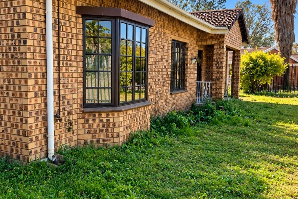 Rear view of a face brick townhouse featuring a bay window, tiled roof, and established garden area.