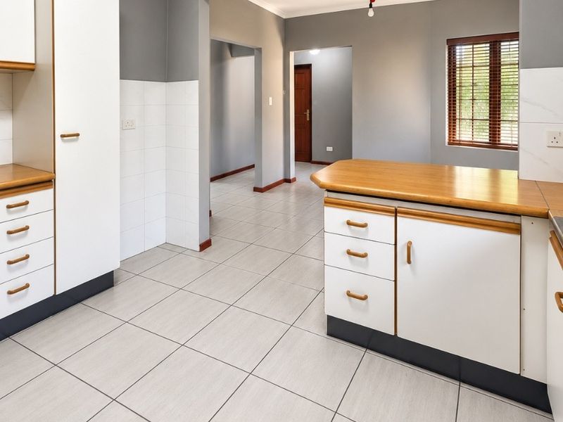 A clean, empty kitchen featuring white cabinetry with wooden countertops, tiled flooring, and a neutral grey wall finish, offering a functional layout.