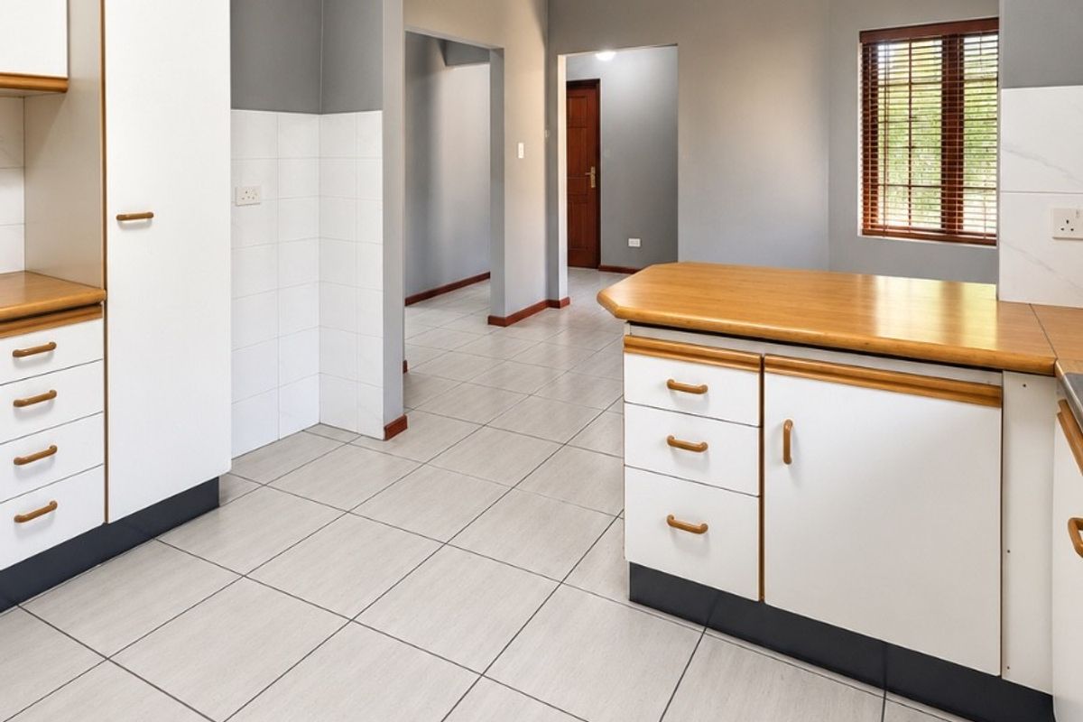 A clean, empty kitchen featuring white cabinetry with wooden countertops, tiled flooring, and a neutral grey wall finish, offering a functional layout.