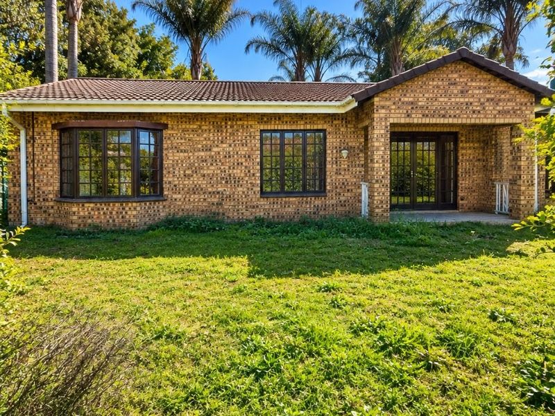 Rear view of a face brick townhouse featuring a covered patio, bay window, and established garden with mature palm trees.