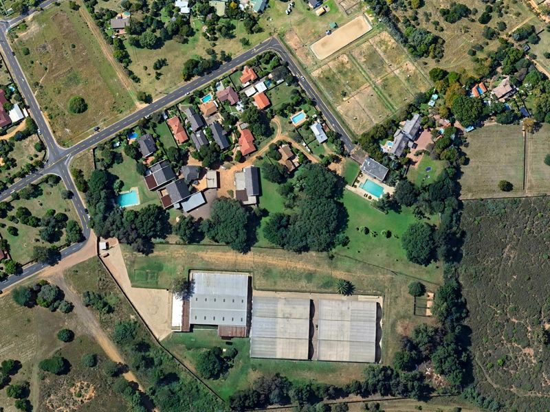 An aerial view of the residential property featuring large industrial-style sheds, expansive grounds, and established trees within a semi-rural neighborhood setting.