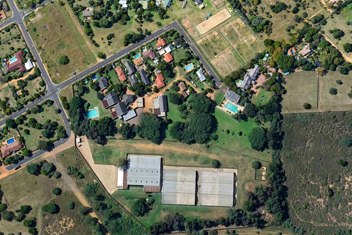 An aerial view of the residential property featuring large industrial-style sheds, expansive grounds, and established trees within a semi-rural neighborhood setting.