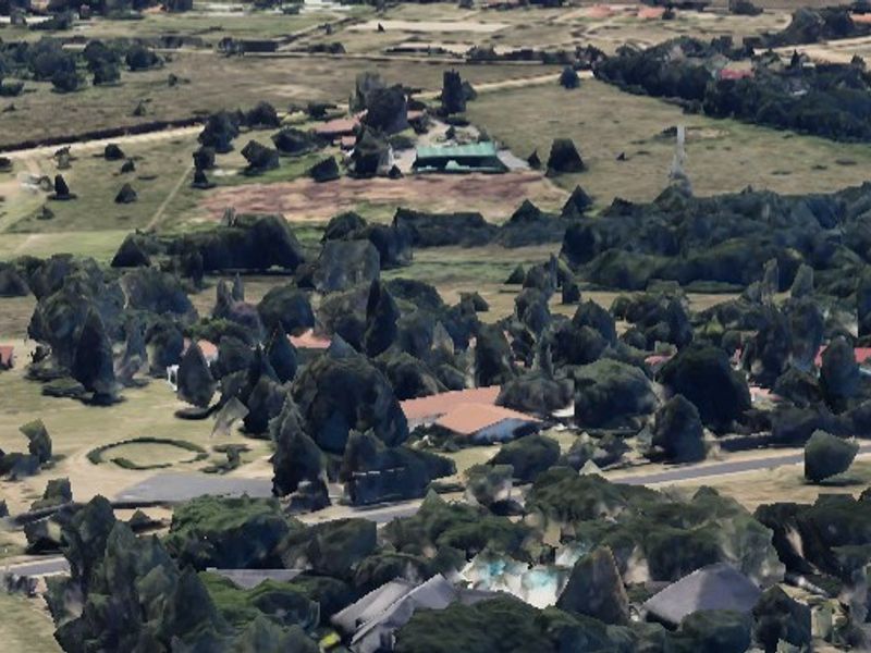 An aerial view of a residential area featuring scattered trees, open land, and local road infrastructure.