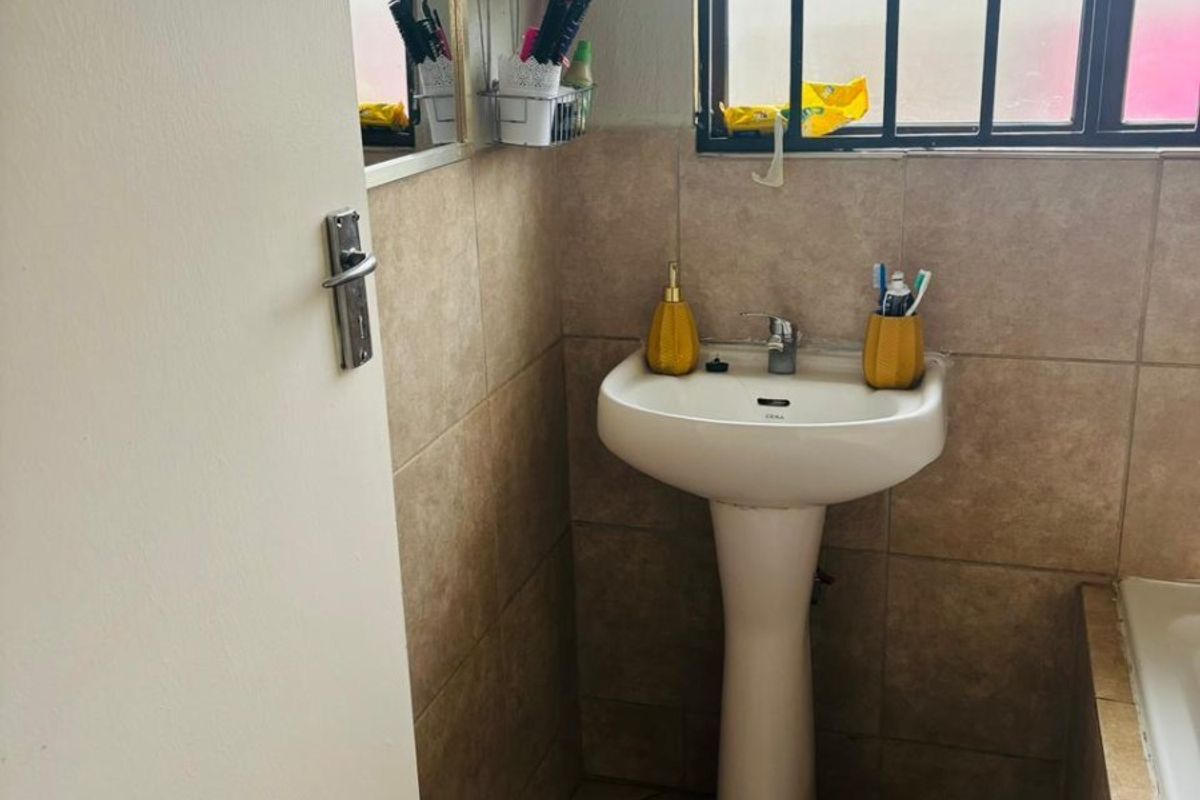 A functional bathroom featuring a pedestal basin, tiled walls and flooring, and a window fitted with a security gate.
