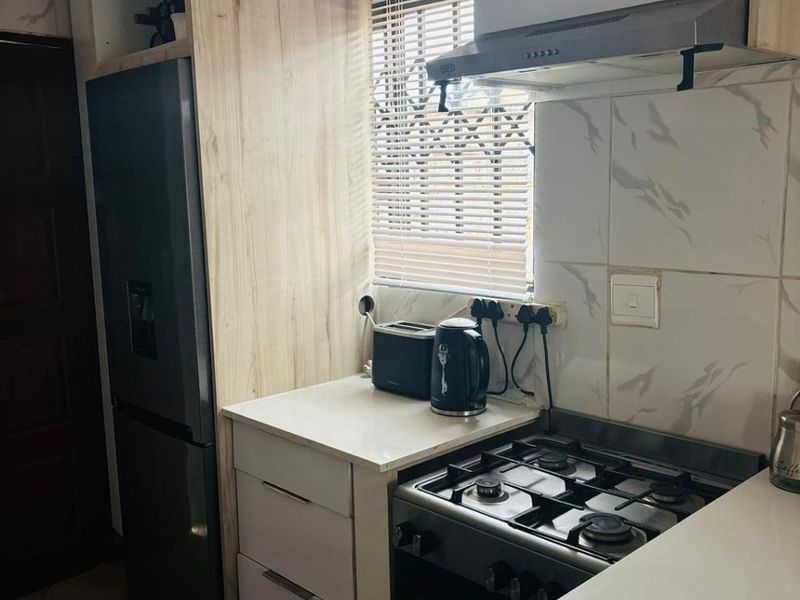 Compact kitchen featuring modern light wood-look cabinetry, marble-style wall tiles, and a built-in gas stove with an extractor fan.