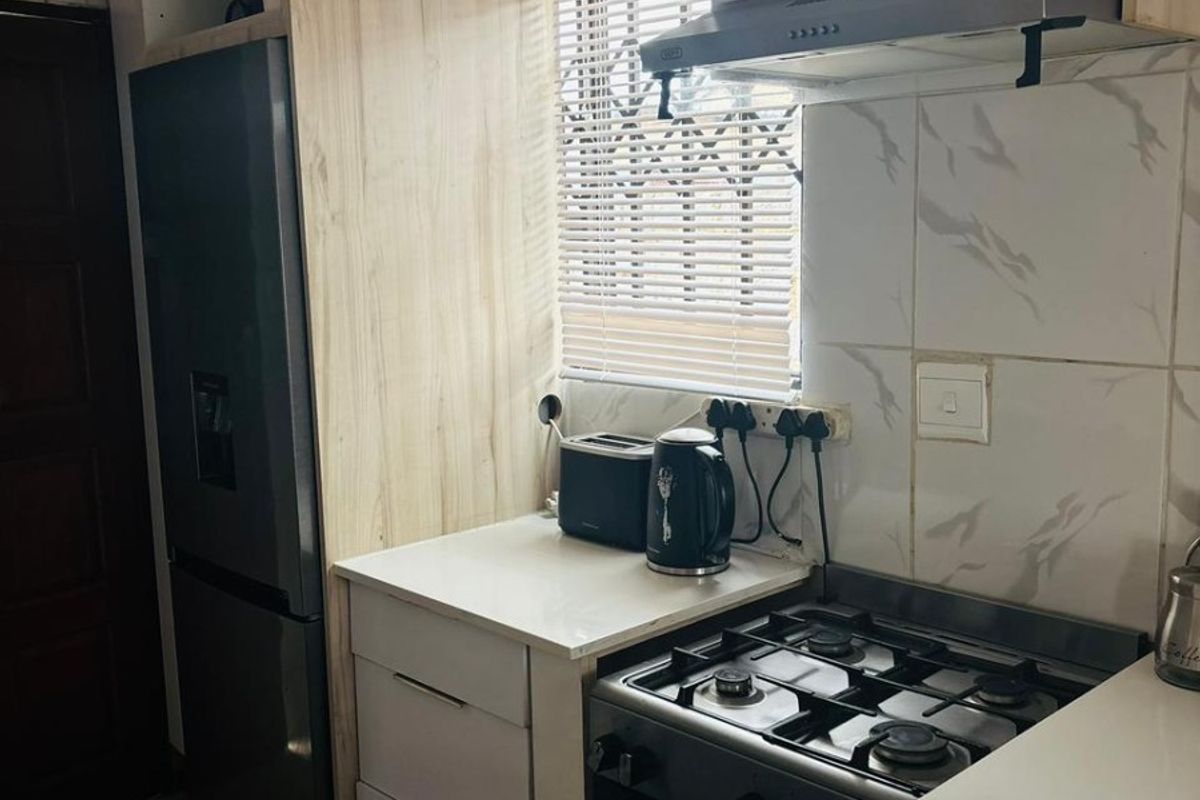 Compact kitchen featuring modern light wood-look cabinetry, marble-style wall tiles, and a built-in gas stove with an extractor fan.