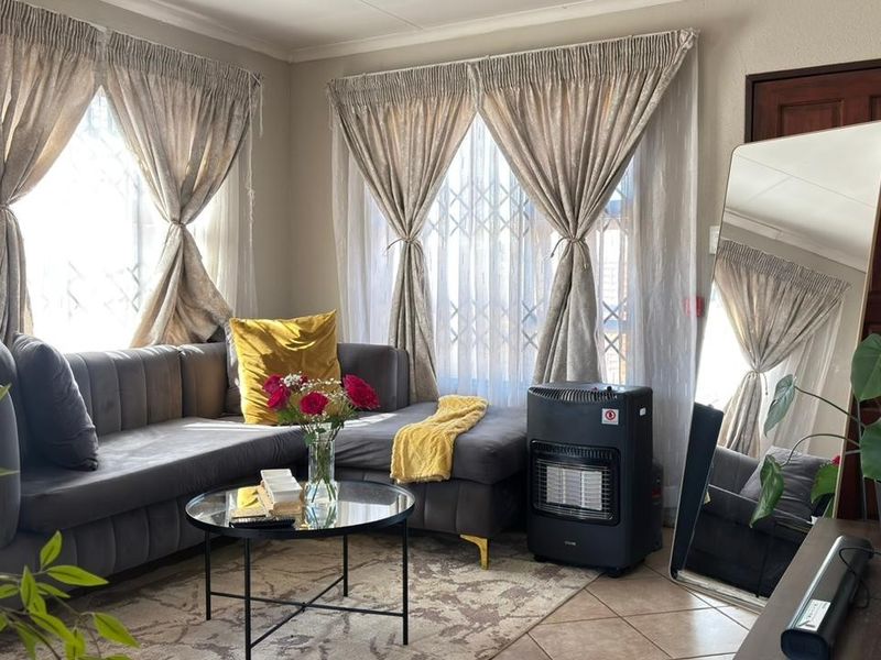 A comfortable living room featuring tiled flooring and large windows fitted with security gates, providing natural light and a secure environment.