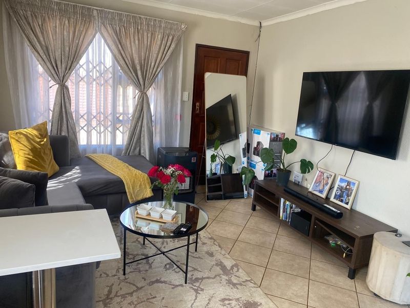 A comfortable living room featuring tiled flooring, a large window with security gate, and a coved ceiling.