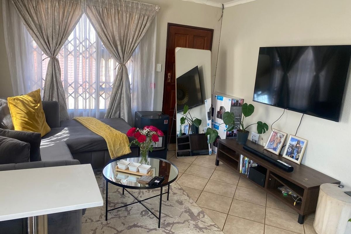 A comfortable living room featuring tiled flooring, a large window with security gate, and a coved ceiling.