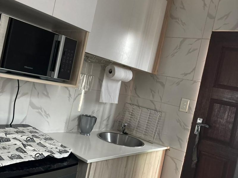 A compact scullery area featuring modern white and wood-grain cabinetry, a stainless steel sink, and marble-effect wall tiling.