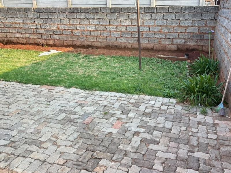 A rear outdoor area featuring a paved patio, a small lawn, and concrete block boundary walls.
